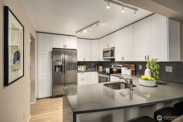 kitchen featuring stainless steel appliances, a peninsula, a sink, decorative backsplash, and dark countertops