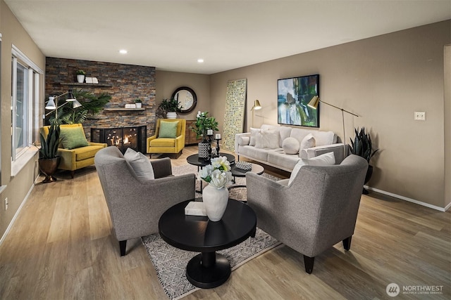 living area featuring baseboards, wood finished floors, and a stone fireplace