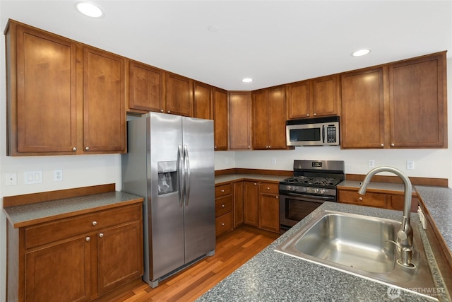 kitchen featuring dark countertops, wood finished floors, appliances with stainless steel finishes, and a sink