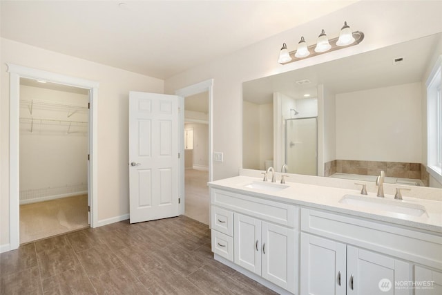 bathroom with double vanity, a spacious closet, a stall shower, and a sink