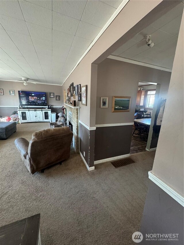 living area with carpet floors, ornamental molding, baseboards, and ceiling fan