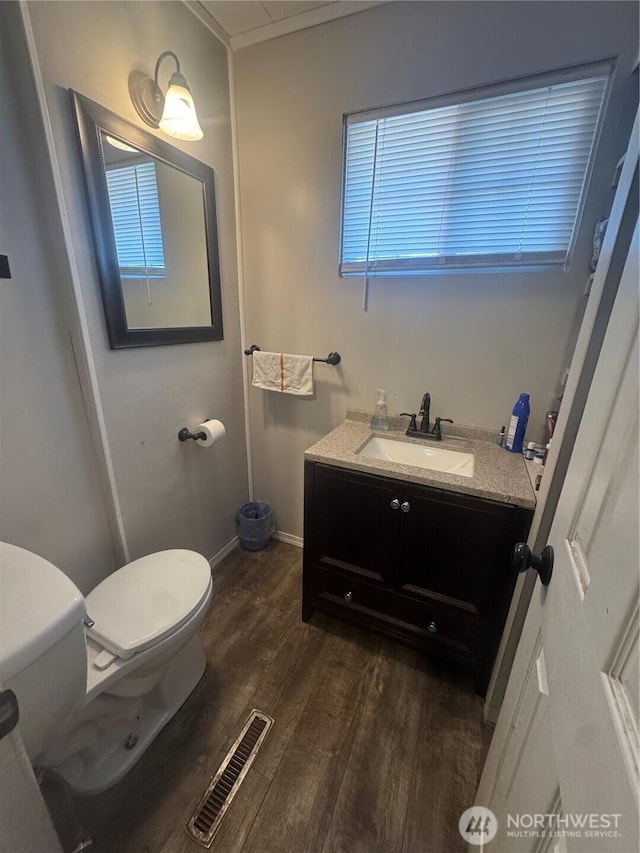 half bathroom with visible vents, toilet, vanity, wood finished floors, and baseboards