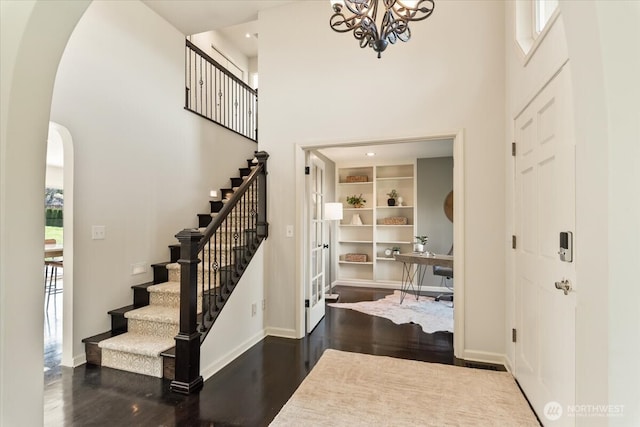 foyer entrance with baseboards, dark wood finished floors, arched walkways, stairs, and a towering ceiling