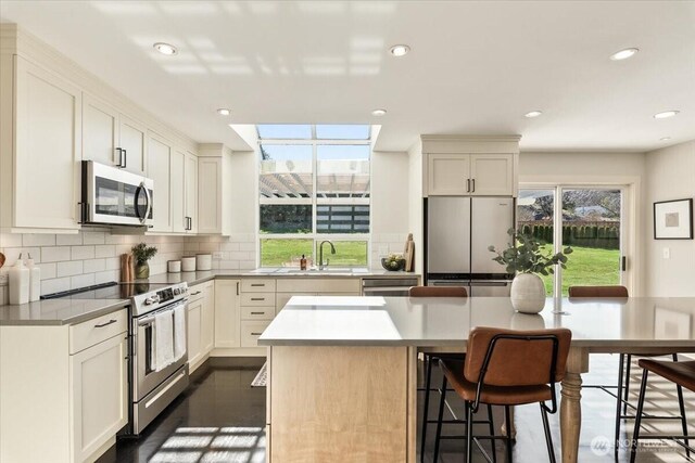 kitchen featuring a kitchen island, a sink, stainless steel appliances, a kitchen breakfast bar, and tasteful backsplash