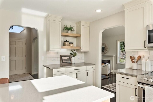 kitchen featuring open shelves, arched walkways, stainless steel appliances, decorative backsplash, and light countertops