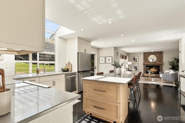 kitchen featuring backsplash, a center island, appliances with stainless steel finishes, light countertops, and a brick fireplace