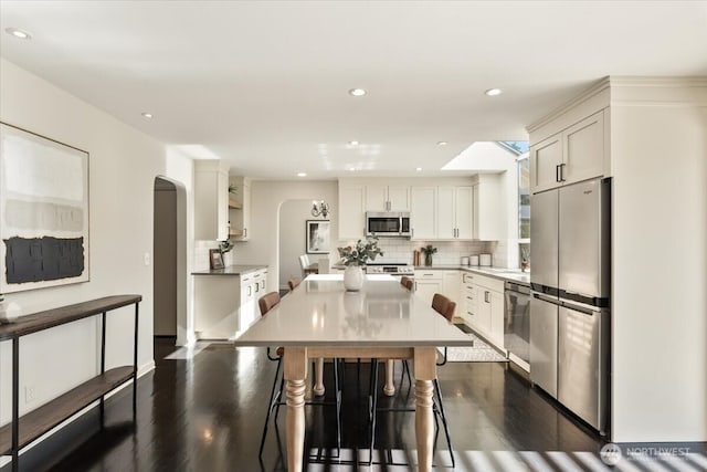 kitchen featuring tasteful backsplash, a center island, white cabinetry, stainless steel appliances, and arched walkways