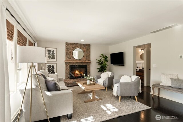 living room featuring a brick fireplace, wood finished floors, and visible vents