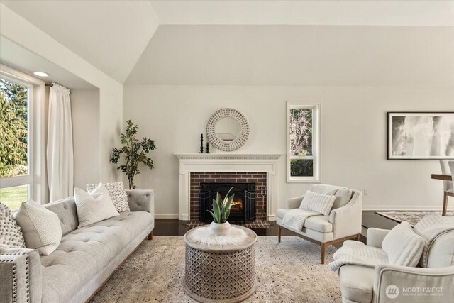 living area with a fireplace, wood finished floors, baseboards, and vaulted ceiling