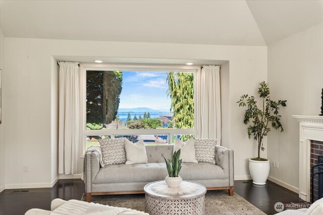 living area featuring vaulted ceiling, a fireplace, baseboards, and wood finished floors