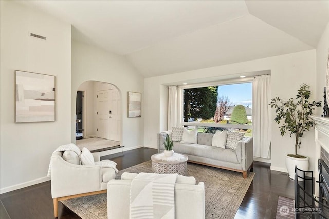 living area with wood finished floors, baseboards, visible vents, arched walkways, and vaulted ceiling