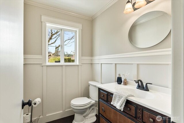 bathroom featuring crown molding, a wainscoted wall, toilet, a decorative wall, and vanity