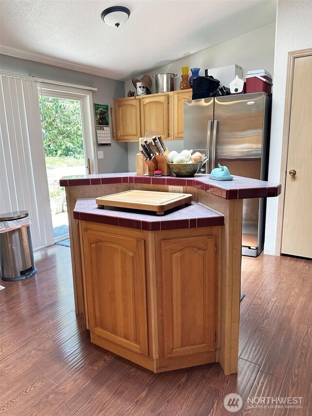 kitchen with tile counters, freestanding refrigerator, a center island, and wood finished floors