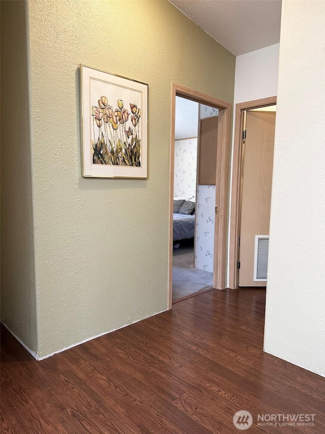 hallway with a textured wall, wood finished floors, and visible vents