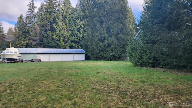 view of yard with an outdoor structure, a wooded view, and an outbuilding