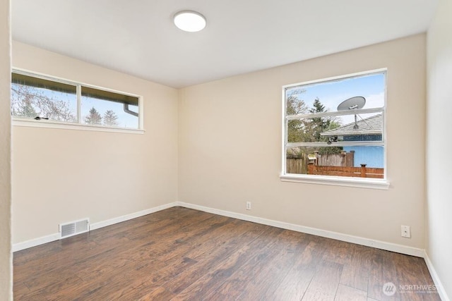 empty room with wood finished floors, visible vents, a wealth of natural light, and baseboards