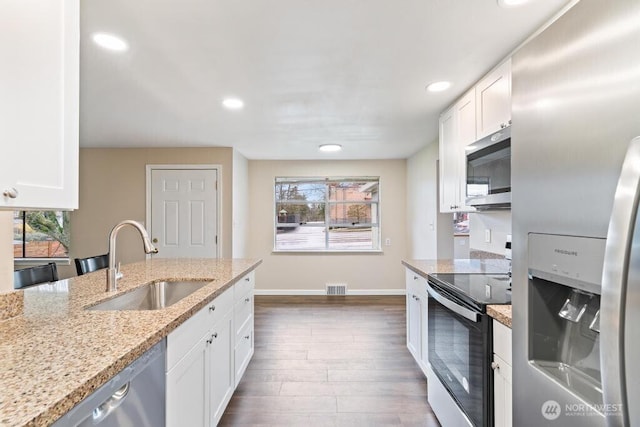 kitchen with a sink, wood finished floors, appliances with stainless steel finishes, and white cabinets