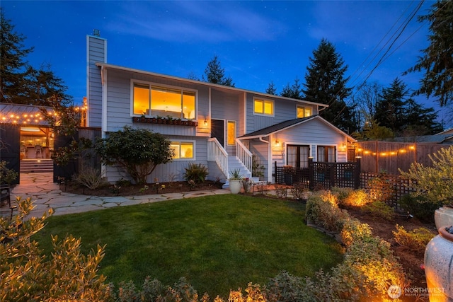 bi-level home with a chimney, fence, and a front lawn