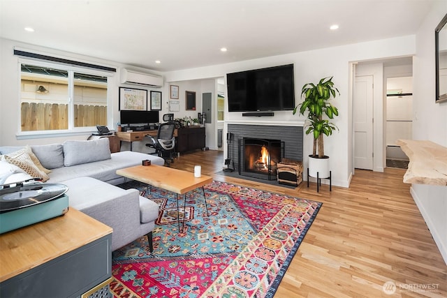 living room featuring recessed lighting, a wall mounted AC, a fireplace with flush hearth, light wood-type flooring, and baseboards