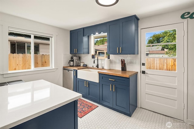 kitchen with decorative backsplash, stainless steel dishwasher, blue cabinetry, wooden counters, and a sink