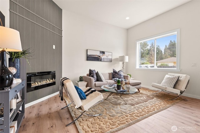 living area featuring a glass covered fireplace, recessed lighting, baseboards, and wood finished floors