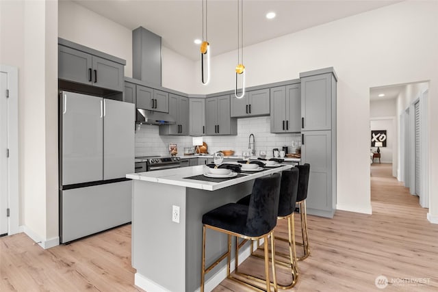 kitchen featuring under cabinet range hood, stainless steel electric range, freestanding refrigerator, decorative backsplash, and light wood finished floors