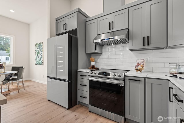 kitchen featuring electric stove, gray cabinets, decorative backsplash, freestanding refrigerator, and under cabinet range hood