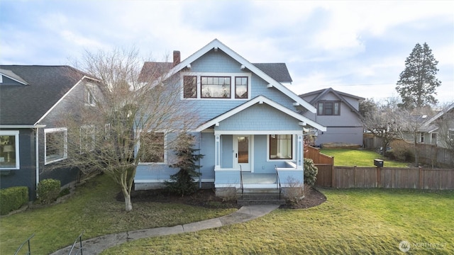 view of front of house with covered porch, a chimney, fence, and a front lawn