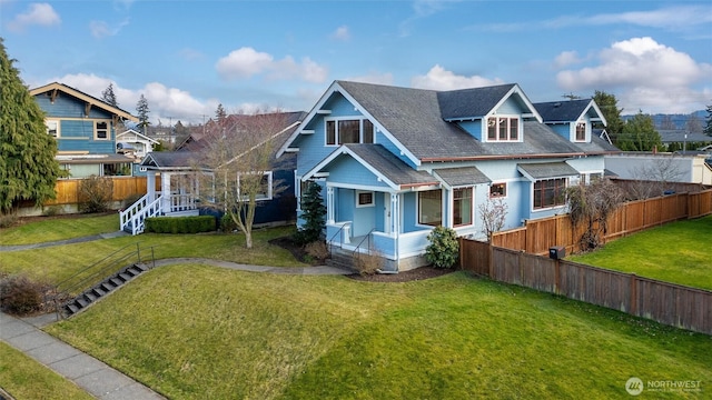 view of front of home with roof with shingles, a front yard, and fence