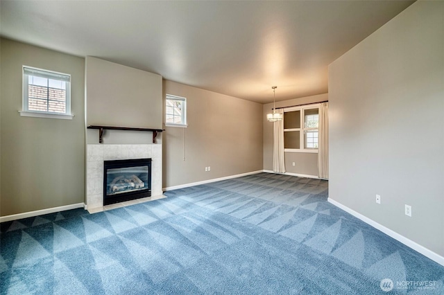 unfurnished living room with a tiled fireplace, dark carpet, an inviting chandelier, and baseboards