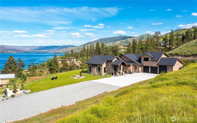 exterior space featuring a garage, a front yard, stone siding, a water and mountain view, and gravel driveway