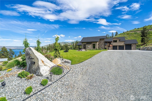 view of front of property featuring a garage, stone siding, gravel driveway, a mountain view, and a front yard