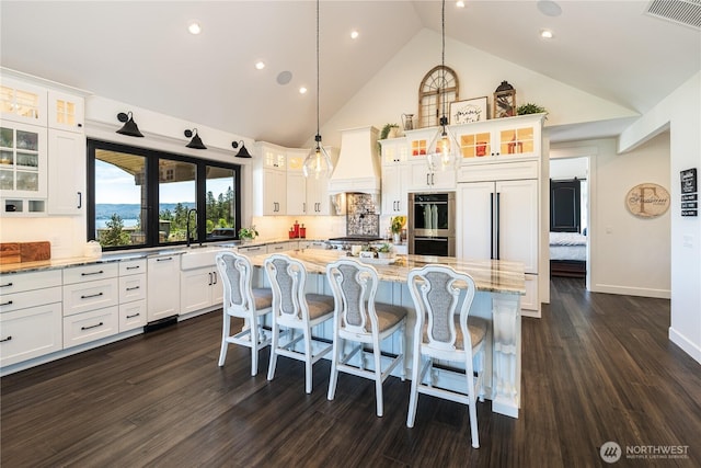 kitchen featuring visible vents, white cabinets, custom range hood, stainless steel appliances, and a sink