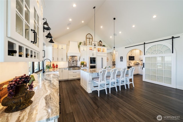 kitchen with arched walkways, a large island, custom exhaust hood, stainless steel appliances, and a sink