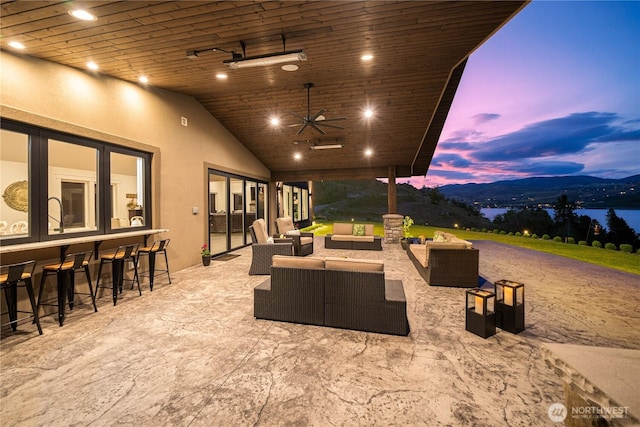 patio terrace at dusk with outdoor dry bar, a mountain view, an outdoor living space, and a ceiling fan