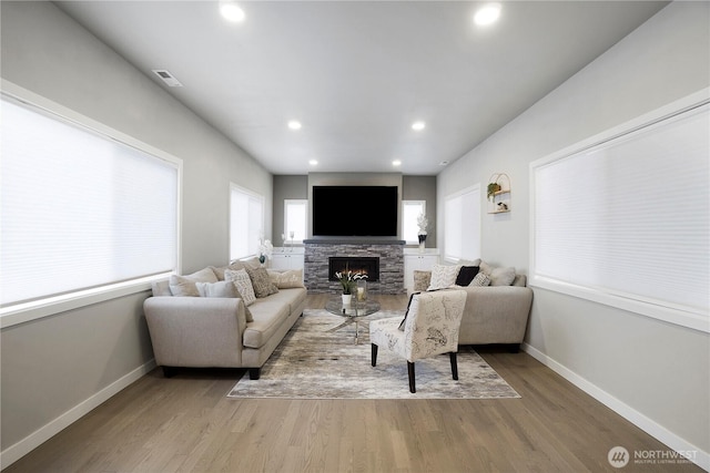 living area featuring recessed lighting, a stone fireplace, baseboards, and wood finished floors