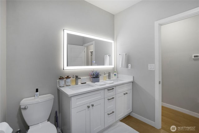 bathroom with baseboards, a sink, toilet, and double vanity