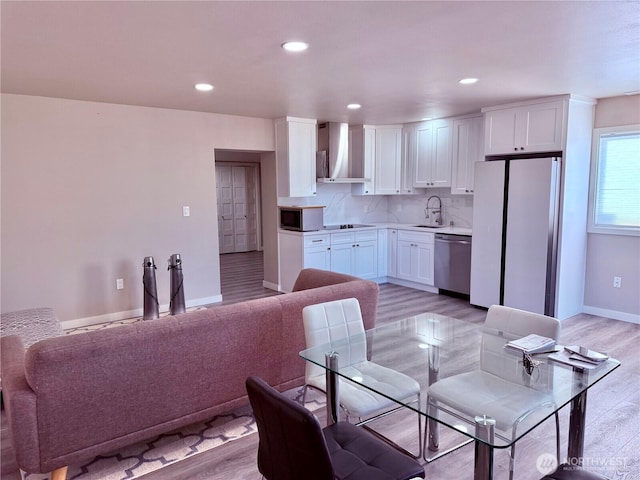 kitchen featuring stainless steel appliances, decorative backsplash, white cabinetry, a sink, and wall chimney range hood