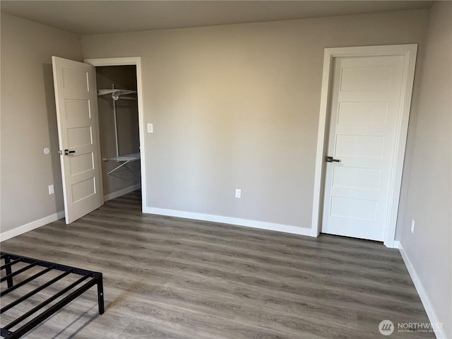 unfurnished bedroom featuring a spacious closet, a closet, wood finished floors, and baseboards