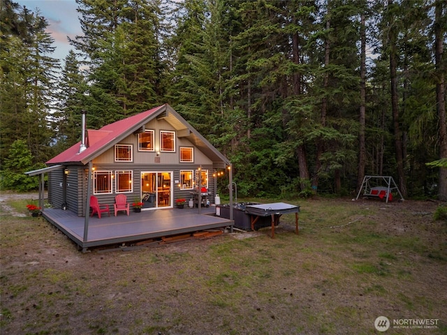 back of house at dusk with a wooded view, metal roof, a lawn, and a wooden deck