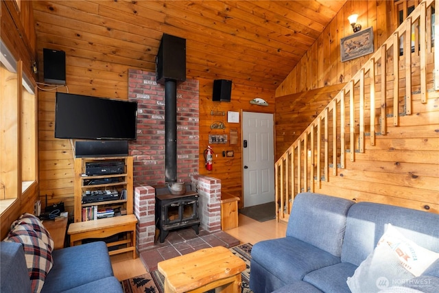 living area with wooden walls, wooden ceiling, a wood stove, stairs, and vaulted ceiling