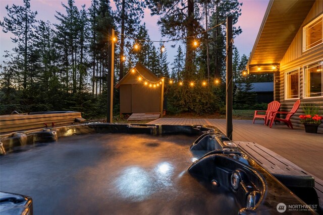 patio terrace at dusk with an outdoor hot tub, a deck, and an outbuilding