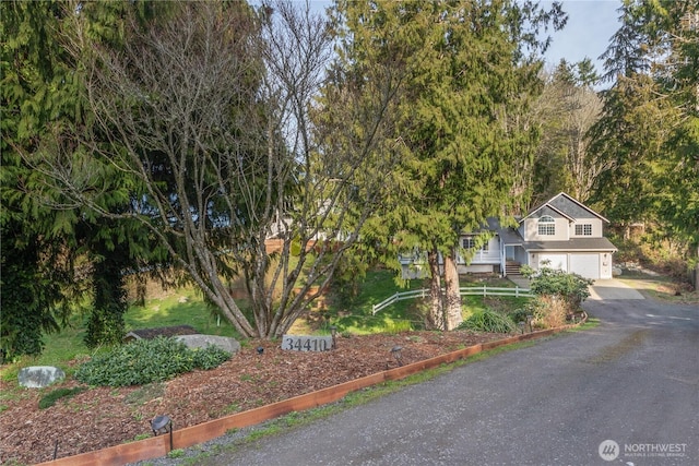 view of property hidden behind natural elements featuring a garage and aphalt driveway