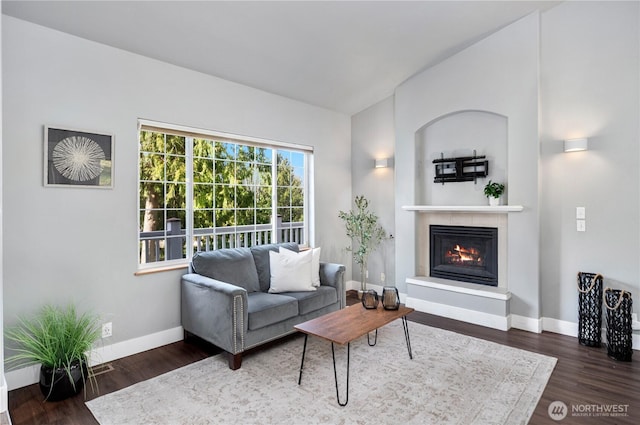 living area with baseboards, vaulted ceiling, wood finished floors, and a glass covered fireplace