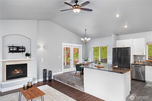 kitchen featuring stainless steel dishwasher, freestanding refrigerator, a center island, dark stone countertops, and dark wood finished floors