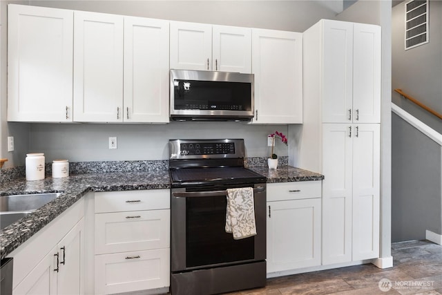 kitchen with appliances with stainless steel finishes, dark stone countertops, wood finished floors, and white cabinetry