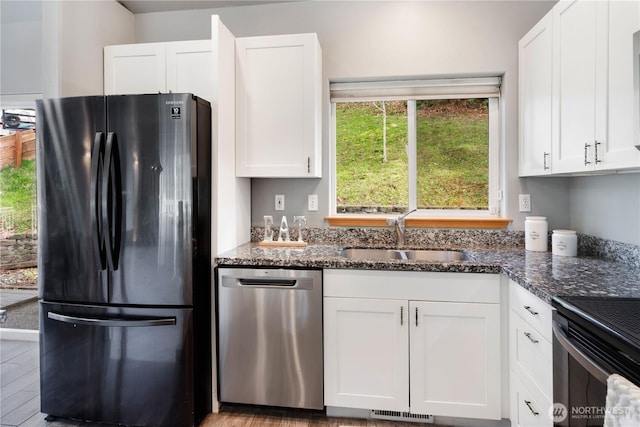 kitchen featuring a sink, white cabinetry, stainless steel dishwasher, freestanding refrigerator, and dark stone counters