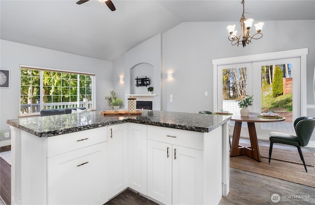 kitchen with lofted ceiling, dark stone countertops, dark wood-style flooring, decorative light fixtures, and a fireplace