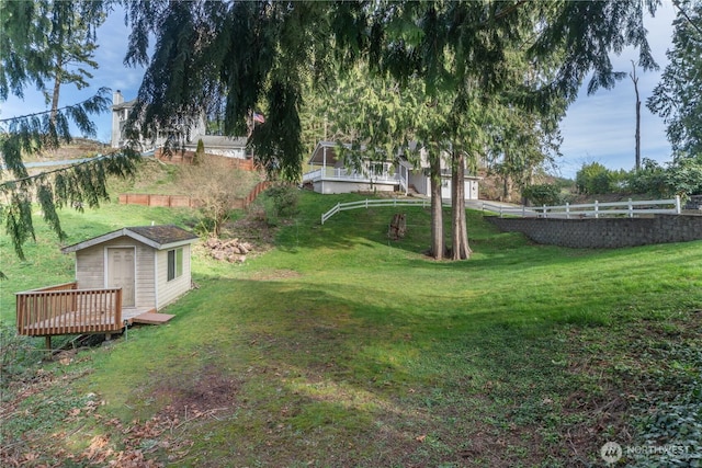 view of yard with a storage unit, an outdoor structure, a deck, and fence