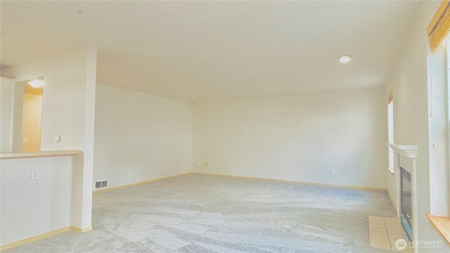 unfurnished room featuring baseboards, a fireplace with flush hearth, visible vents, and carpet flooring